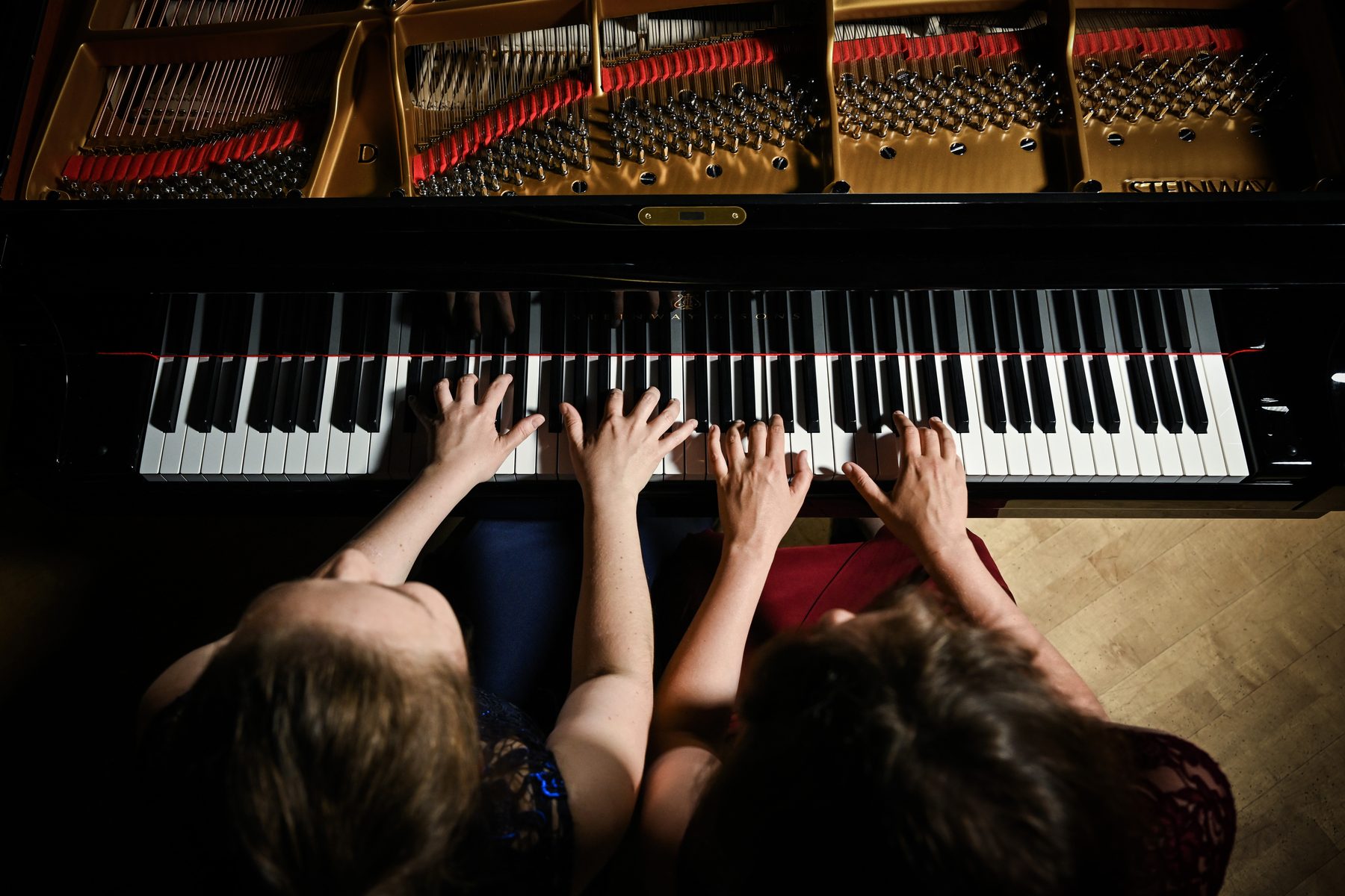Vier Hände auf der Klaviatur eines Steinway-Flügels, von oben